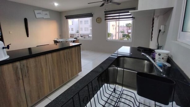 A modern kitchen with a black countertop, wooden cabinets, a stainless steel sink, and a ceiling fan.