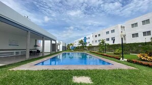 A modern building with a swimming pool surrounded by well-maintained grass and plants.