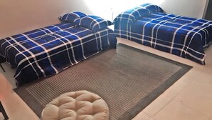 A room with two beds, a rug, and a round ottoman.