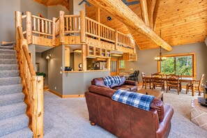 A spacious living area with a wooden staircase, a leather sofa, a dining table, and a kitchen area. - Mountain Escape by Terry Peak (Lead)