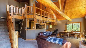A rustic cabin interior with a wooden staircase, a loft bedroom, a dining area, and a living room with a leather couch. - Mountain Escape by Terry Peak (Lead)