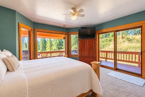 A bedroom with a bed, a television, and a view of a deck and trees. - Mountain Escape by Terry Peak (Lead)