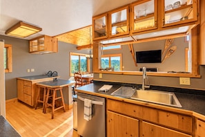 A modern kitchen with wooden cabinets, a stainless steel sink, and a dining area with a view of the outdoors. - Mountain Escape by Terry Peak (Lead)