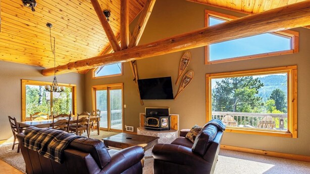 A spacious living room with a fireplace, leather sofas, a dining area, and large windows offering a view of the outdoors. - Mountain Escape by Terry Peak (Lead)