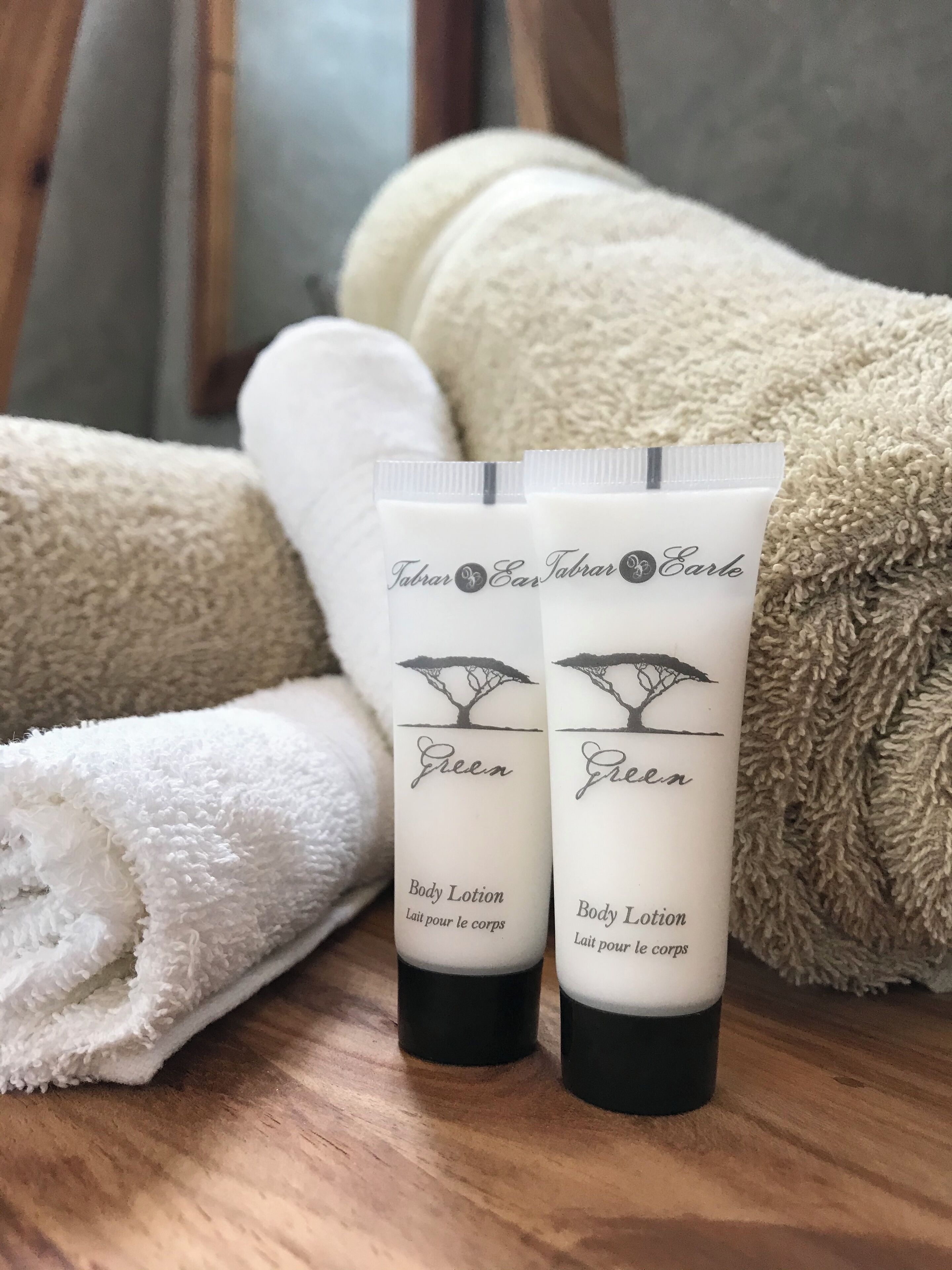 Twee tubes bodylotion, gelabeld 'Green', op een houten oppervlak met opgerolde witte handdoeken op de achtergrond.