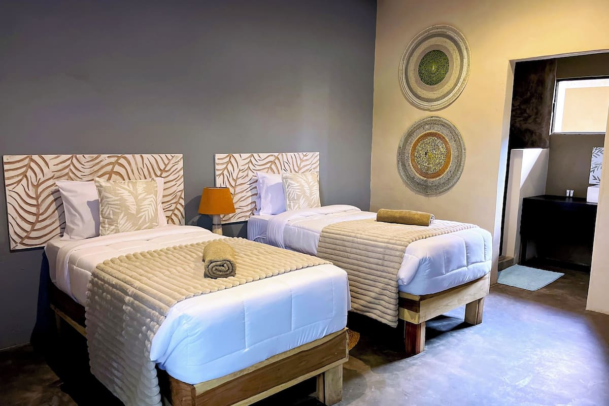 A hotel room with two beds, a nightstand, decorative wall art, and a view of the outside.