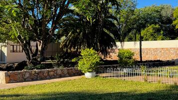 A well-maintained garden with a stone wall, a metal fence, and a variety of trees and shrubs.