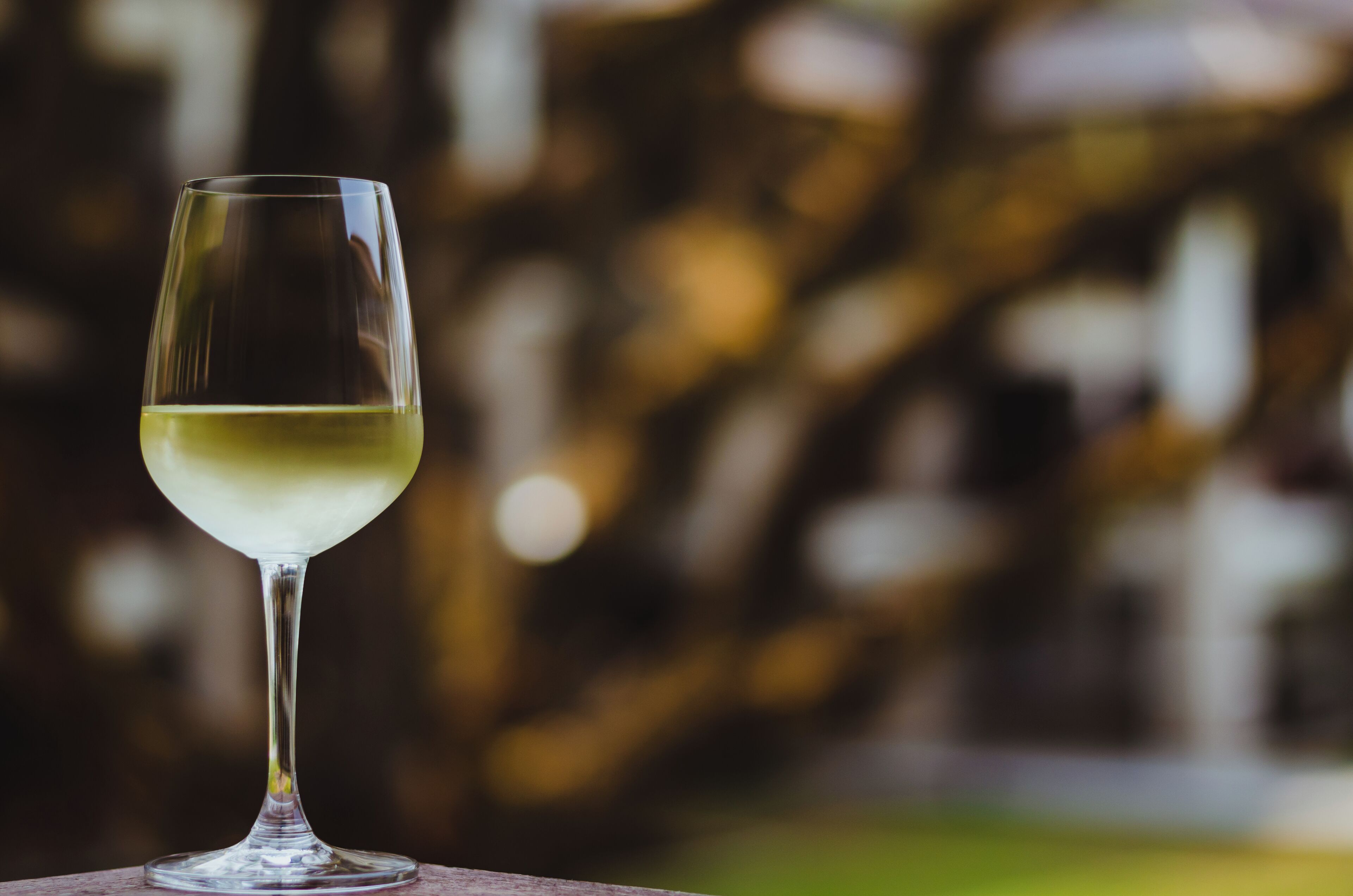 Una copa de vino blanco transparente sobre una mesa, con un fondo borroso de edificios.