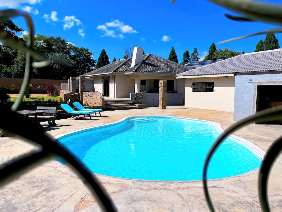 A swimming pool with lounge chairs, a stone wall, and a house with a tiled roof.