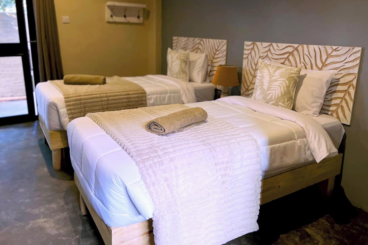 Two double beds with white bedding and a rolled towel on the bed in the foreground.