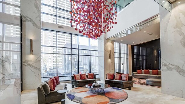A spacious lobby with large windows, a central seating area with sofas and a coffee table, and a unique hanging installation. - High End 6 people Apartment Islington Etobicoke (Toronto)