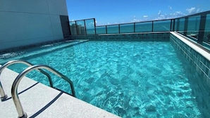 A clear blue infinity pool with metal railings, a tiled edge, and a view of the ocean. - Smart Stay Apto 904-Mandi Hospitalidade (Maceió)