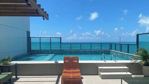 An outdoor swimming pool with a view of the ocean, a wooden pergola, and a lounge chair. - Smart Stay Apto 904-Mandi Hospitalidade (Maceió)