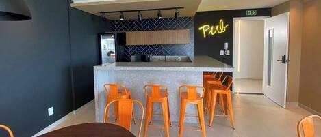 A modern kitchen with a bar area, bar stools, and a neon sign reading "Pub".