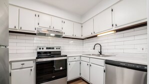 A modern kitchen with white cabinets, a stainless steel oven, a dishwasher, and a tiled backsplash. - Furnished Resort Style Apartment w/ WIFI & Parking (Columbus)