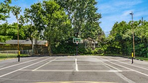 An outdoor basketball court with a green basketball hoop, surrounded by trees and a fence. - Furnished Resort Style Apartment w/ WIFI & Parking (Columbus)