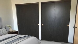 A bedroom with a bed, two dark doors, a nightstand with a vase, and a patterned carpet. - Furnished Resort Style Apartment w/ WIFI & Parking (Columbus)