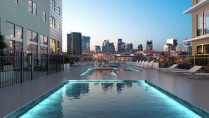 A rooftop pool area with a city skyline view, modern buildings, and a well-lit pool.