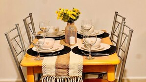 Una mesa de comedor dispuesta con platos blancos, servilletas negras y copas de vino transparentes. En el centro, un florero tejido con flores amarillas.