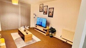 Una sala de estar con televisor, muebles de madera, un radiador y cuadros en la pared.