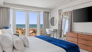 Une chambre d’hôtel avec un grand lit, une télévision, une commode et une vue sur l’océan.