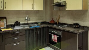 Een moderne keuken met donkere kastjes, een granieten aanrechtblad, roestvrijstalen apparatuur en verlichting onder de kastjes.