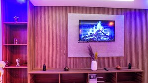 Een moderne woonkamer met een flatscreen televisie aan een houten wand, een houten dressoir eronder en een vaas met gedroogde planten op het dressoir.