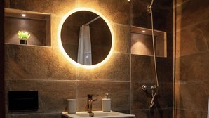 Een moderne badkamer met een ronde spiegel, een houten wastafelmeubel, een toilet en een douche.