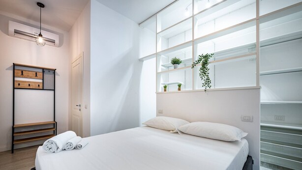 Ein modernes Hotelzimmer mit einem großen Bett, einer Holzregaleinheit und einem Fenster mit Regalen.