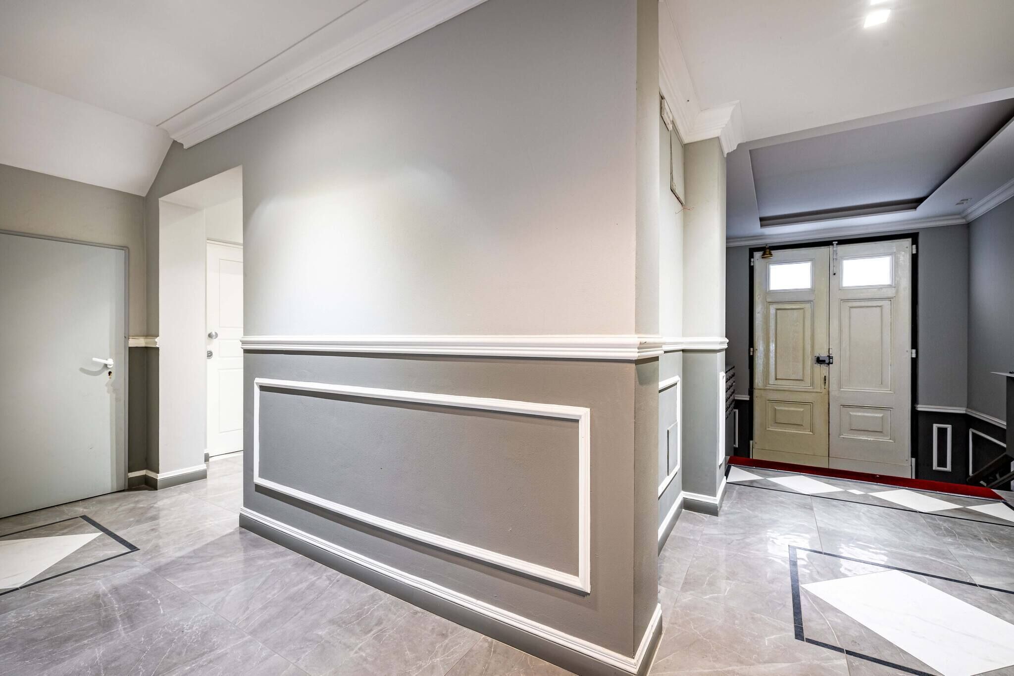 A spacious hallway with a marble floor, a large white accent wall, and a door leading to another room.