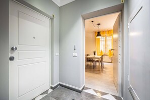 A hallway with a white door, a dining area with yellow chairs, and a chandelier.