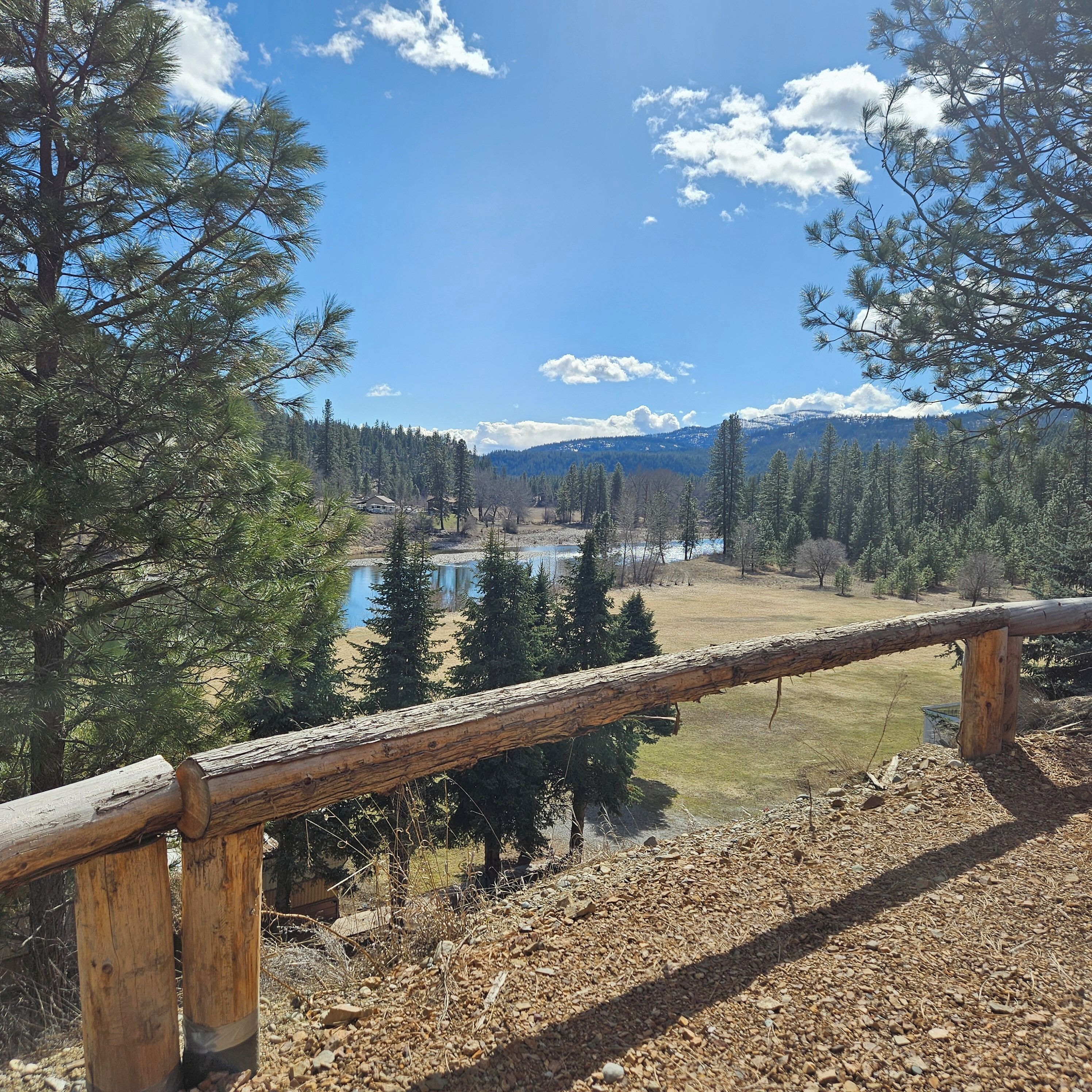 A wooden fence overlooking a lake with trees and mountains in the background.