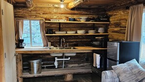 A rustic cabin interior with a wooden floor, a kitchenette with a sink and stove, a refrigerator, a television, and a sofa.