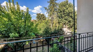 Un balcon donnant sur un jardin, avec un mur en pierre et une rambarde en métal.