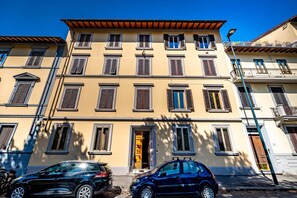 A multi-story building with a yellow facade, multiple windows with shutters, and a visible door. - YiD Aleardi luminous and comfy (Firenze)