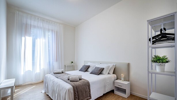 Une chambre à coucher moderne avec un grand lit, des tables de chevet, une armoire et une fenêtre agrémentée de rideaux légers.
