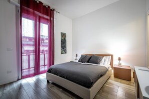 Una camera da letto con un letto, un comodino, una lampada, una finestra con tende e un quadro appeso al muro.