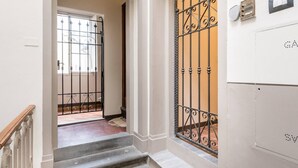Un escalier menant à une porte surmontée d’un portail en fer forgé, avec un interrupteur et un thermostat fixés au mur.