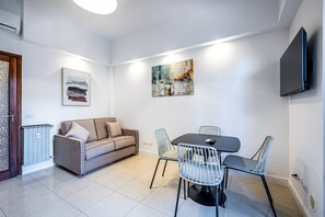 Een moderne woonkamer met een bank, een eettafel en stoelen. Aan de muur hangt een flatscreen-televisie.