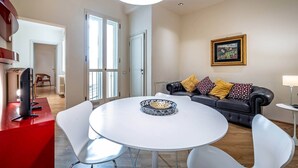 Un salon moderne avec une table ronde blanche, un canapé en cuir noir agrémenté de coussins à motifs, un tableau encadré au mur et un mur d’accent rouge.