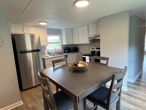 Een moderne keuken met witte kasten, roestvrijstalen apparatuur, een eettafel met stoelen en een raam dat voor natuurlijk licht zorgt.