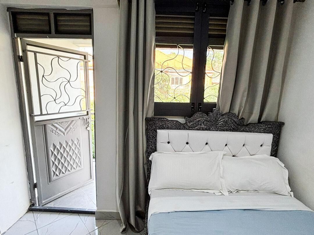 Une chambre à coucher avec un lit, des rideaux, une fenêtre et une porte agrémentée d’un paravent décoratif.