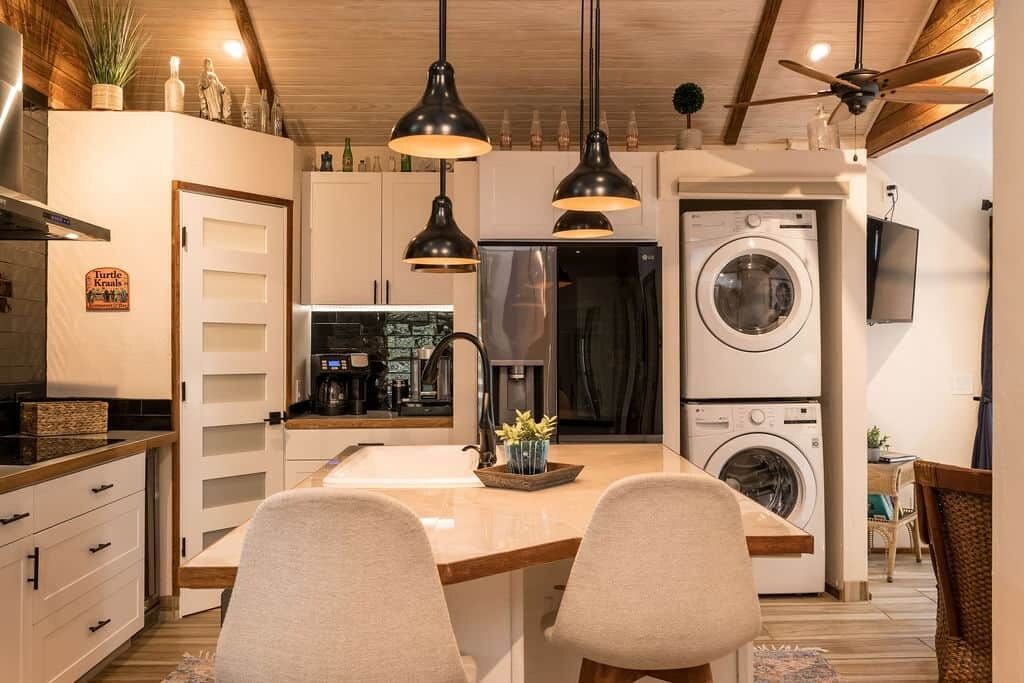 A modern kitchen with a central island, two pendant lights, a ceiling fan, and a built-in washing machine.