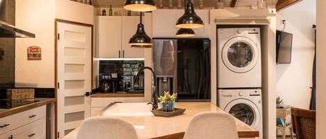 A modern kitchen with a central island, two pendant lights, a ceiling fan, and a built-in washing machine.