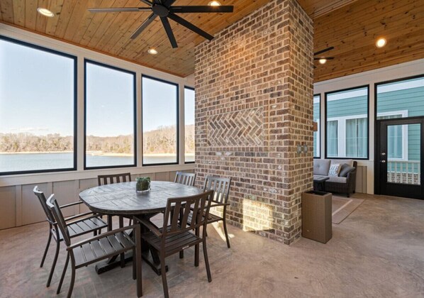 A dining area with a brick fireplace, large windows, and a ceiling fan.