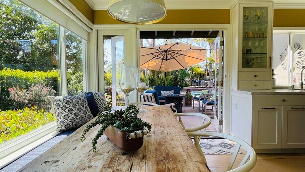 A sunlit room with a wooden table, a window with a view of a garden, and a dining area with outdoor seating. - Gorgeous Solana Beach 3 bd pool, view, perfect for beach & racetrack  (Solana Beach)