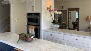 A kitchen with white cabinets, a double oven, a marble countertop, hanging pendant lights, and a vase with orchids. - Gorgeous Solana Beach 3 bd pool, view, perfect for beach & racetrack  (Solana Beach)
