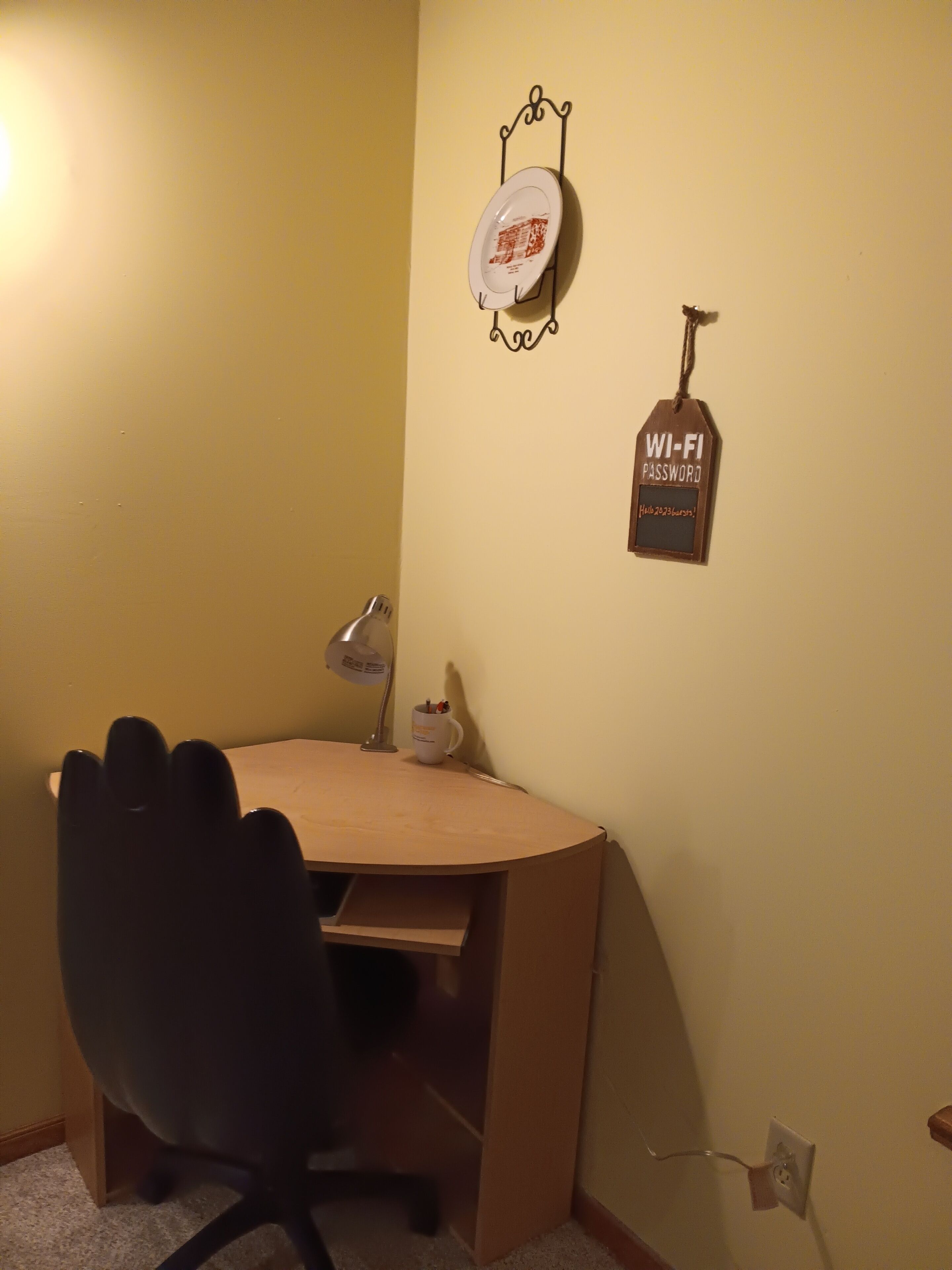 A small office space with a desk, chair, and a wall-mounted Wi-Fi password sign.