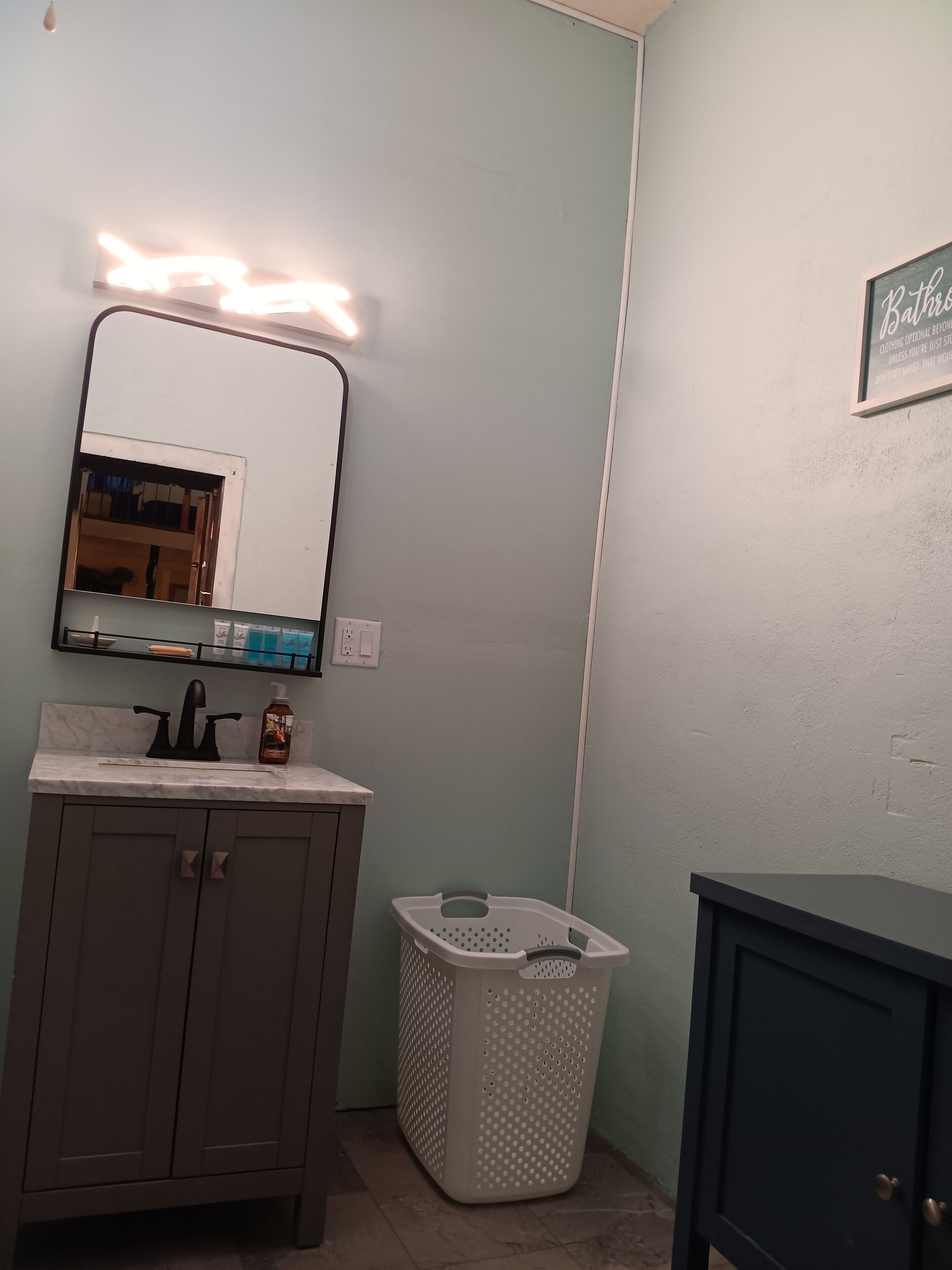A bathroom with a sink, mirror, and a laundry basket.