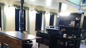 A compact kitchen with a stove, oven, and microwave. There is a wooden table and a trash bin. The room has a balcony with a railing. - Bank on it! Suite Bank (Sidney)